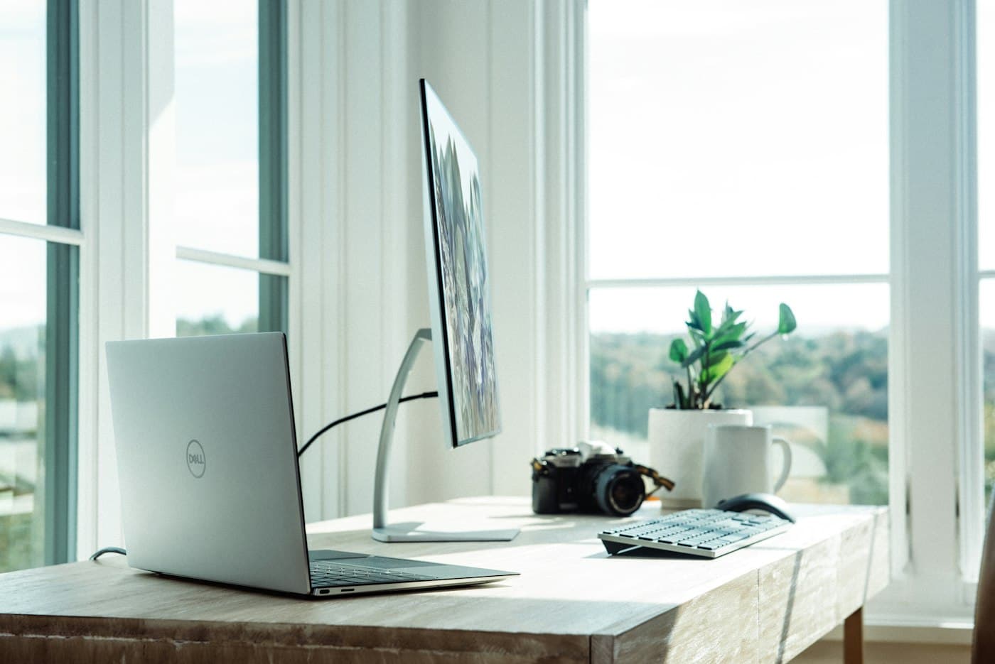 Laptop and monitor on a tidy desk beside a bright window